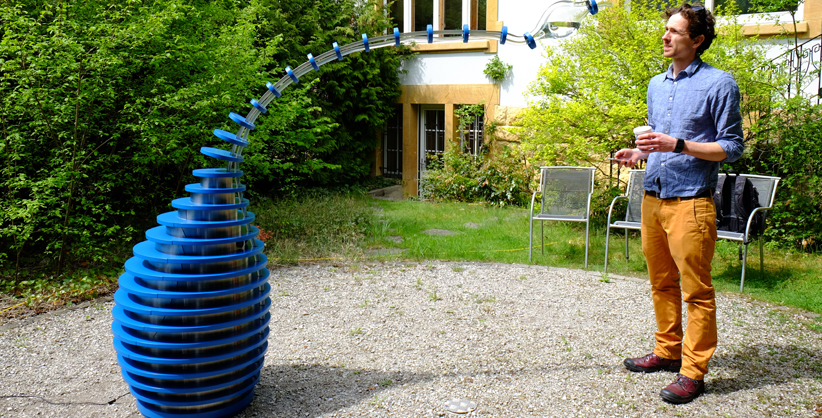 Der Sensor im Objekt nimmt eine Person in der nahen Umgebung wahr. Der Schlauch beugt sich langsam zur Person hin, die einen Becher in der Hand halten sollte. Die Karaffe am Ende des Schlauches neigt sich mit dem Gewicht des Wassers so weit, bis das Wasser aus dem Behälter im Objekt in den Becher der Person fliesst. 