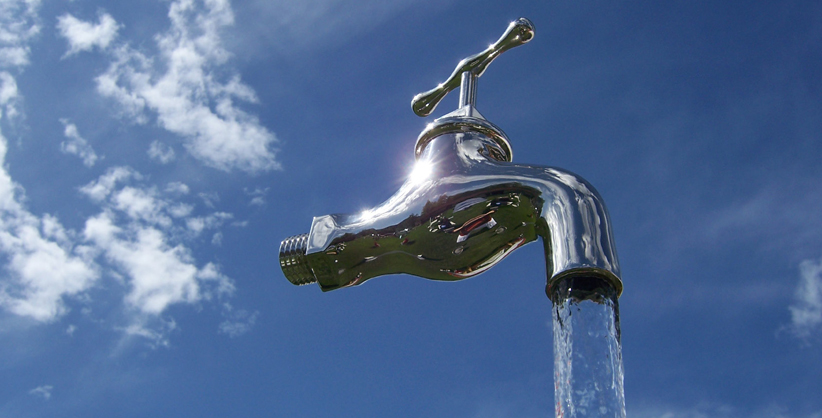 Eine Pumpe bringt Wasser in einer Plexiglasröhre zum Wasserhahn hinauf, Wasser fliesst ausserhalb der Plexiglasröhre in einen Behälter hinunter. 