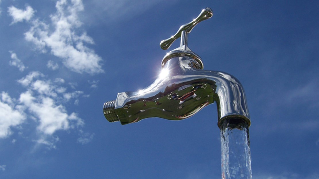 Eine Pumpe bringt Wasser in einer Plexiglasröhre zum Wasserhahn hinauf, Wasser fliesst ausserhalb der Plexiglasröhre in einen Behälter hinunter. 